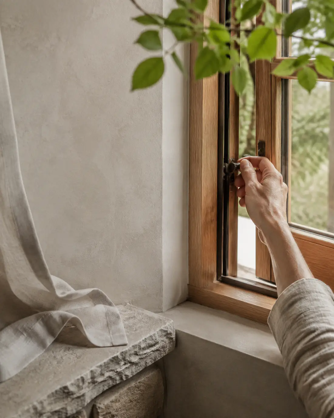 A hand opens a timber-framed window above a textured stone sill