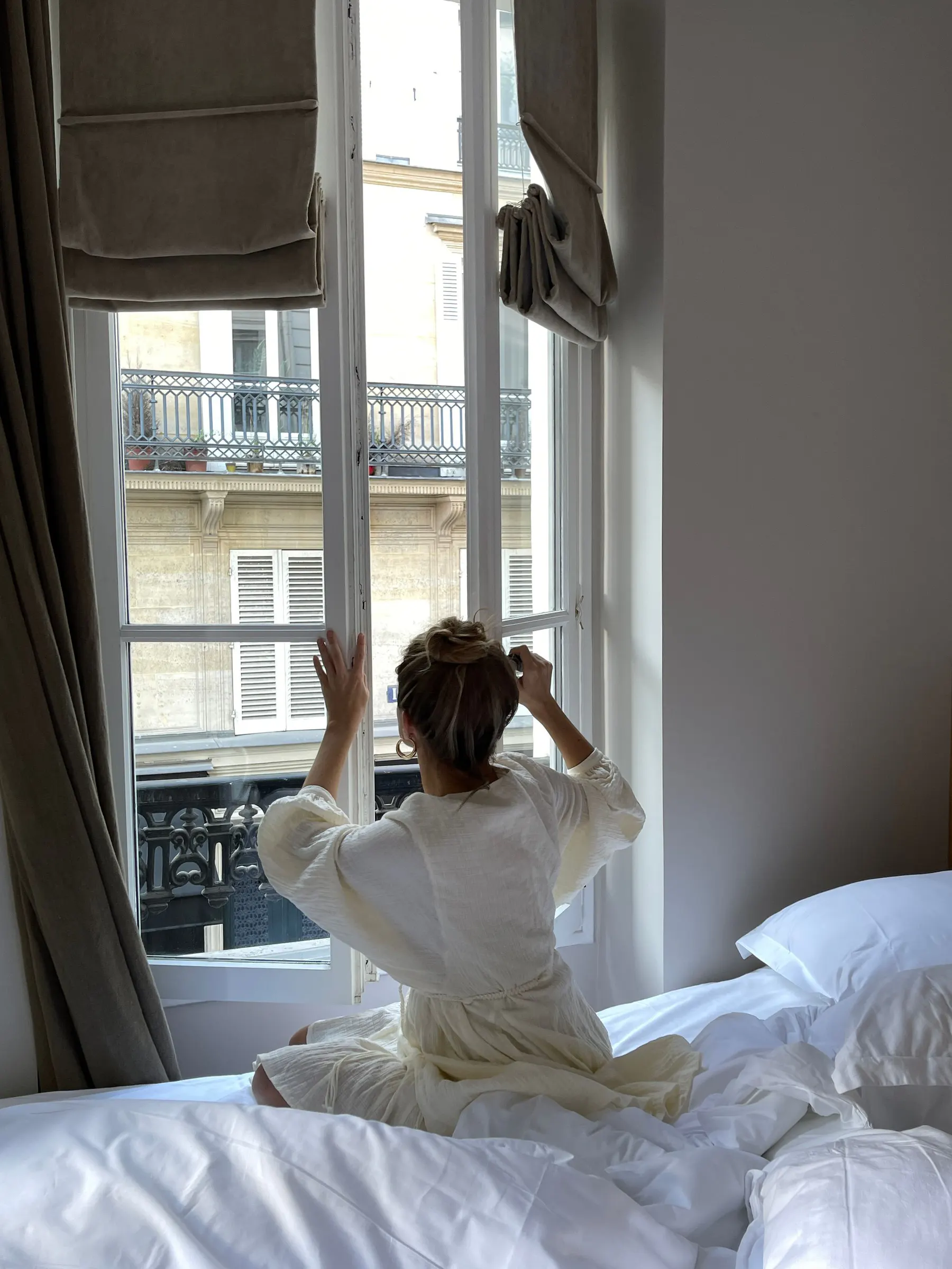 A woman opens a bedroom window to the morning air